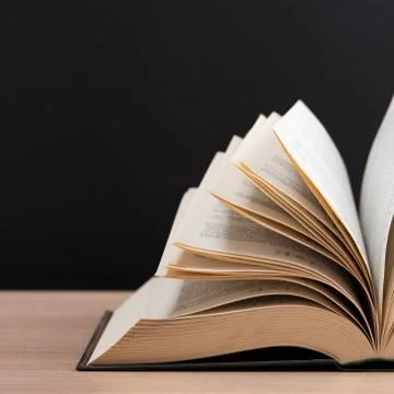 The book is open, lying on the table, sheets fanned out on a black background Stock Photos