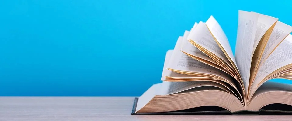 The book is open, lying on the table, sheets fanned out on a blue background. Stock Photos