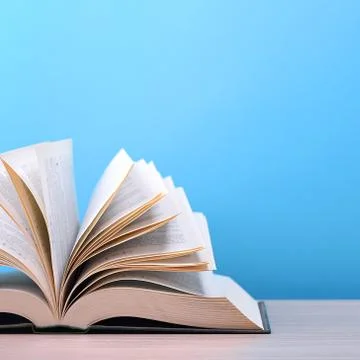 The book is open, lying on the table, sheets fanned out on a blue background. Stock Photos