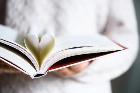 Book with opened pages and shape of heart in girl hands. Copy space. Love Stock Photos