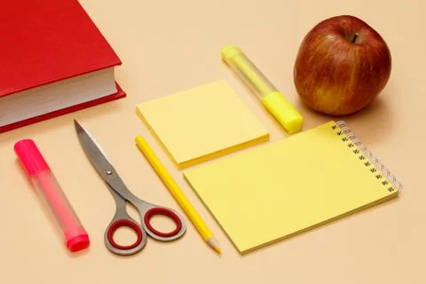 Book, scissors, pencil, notebook, note-paper, felt-tip pens and apple on beig Stock Photos