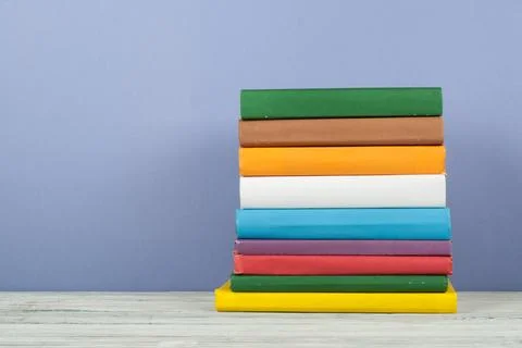 Book stack, hardback colorful books on wooden table and blue background. Back Stock Photos