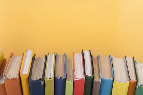 Book stacking. Open hardback books on wooden table and yellow background. B.. Stock Photos