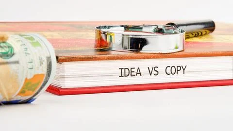 A book titled Idea vs Copy is placed on a table with a magnifying glass and s Stock Photos