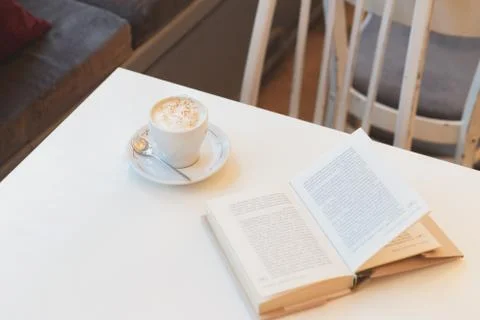 Book on white table with cup of coffee in cafe Stock Photos