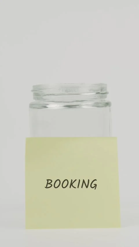 Booking text or word on yellow sticky note attached to glass jar with hand Stock Footage 311683195