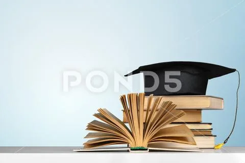 Books and mortarboard on wooden table Stock Photos