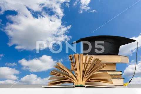 Books and mortarboard on wooden table Stock Photos