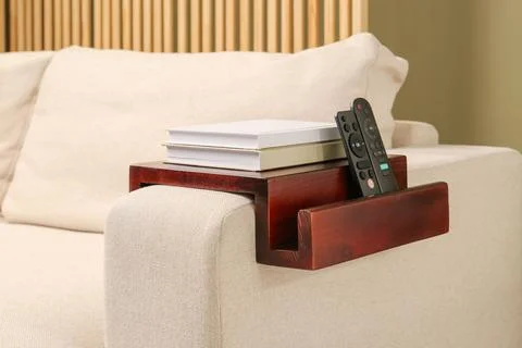 Books and remote controls on sofa armrest wooden table in room. Interior el.. Stock Photos