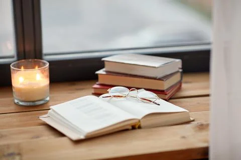Books, glasses and candle burning on window sill Stock Photos