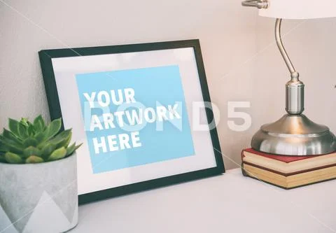 Books with picture frame and pot plant on table PSD Template