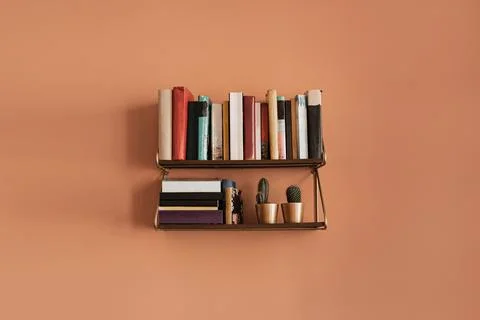 Books stack on hanging shelf. Coral peach wall background. Aesthetic minimal  Stock Photos