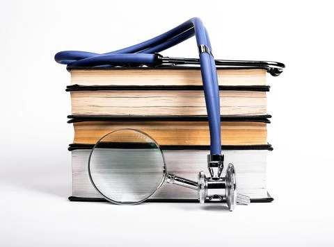 Books stack with stethoscope and magnifying glass. Medical data search and Stock Photos