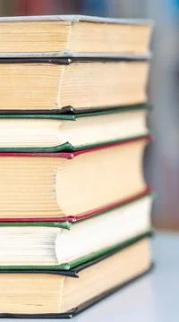 Books stack on wooden table and blurred bookshelf in library hall Stock Photos