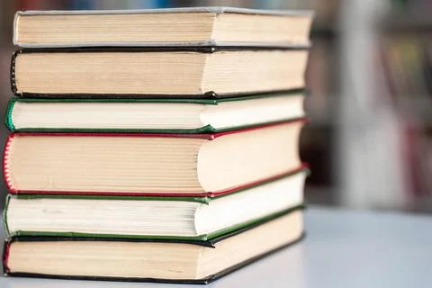 Books stack on wooden table and blurred bookshelf in library hall Stock Photos
