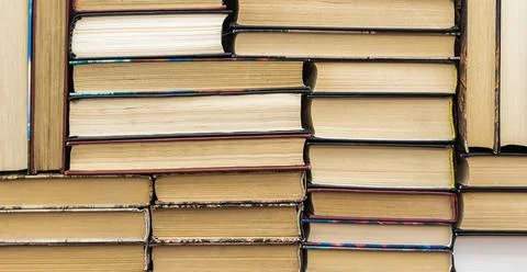 Books stack on wooden table and blurred bookshelf in library hall. Stock Photos