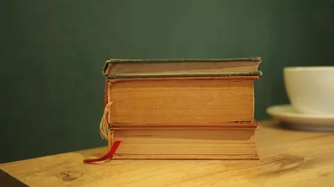 Books stacked on a table with a cup in the background Stock Footage 339996895