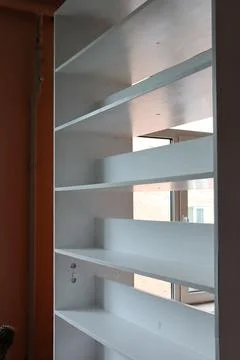Bookshelf with empty shelves next to a window in a room with orange walls during 写真素材