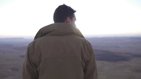 Boom up to a man looking around on a desert mountain in the morning Stock Footage 73080020