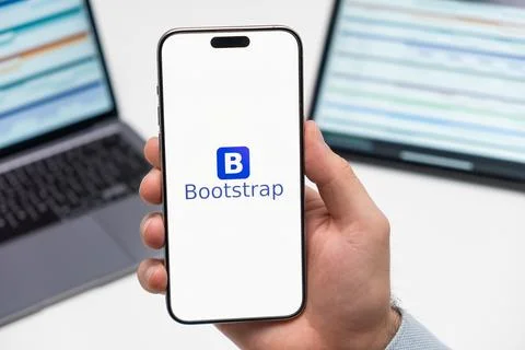 Bootstrap logo on the screen of smartphone in mans hand on the workplace Stock Photos