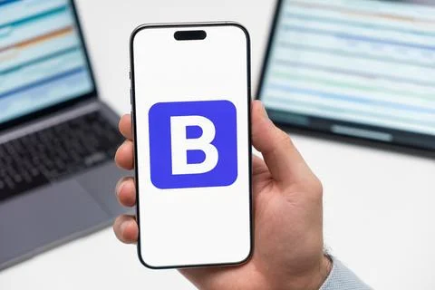 Bootstrap logo on the screen of smartphone in mans hand on the workplace Stock Photos