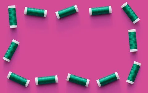 Border of flat-lying spools of green thread on pink background Stock-Fotos