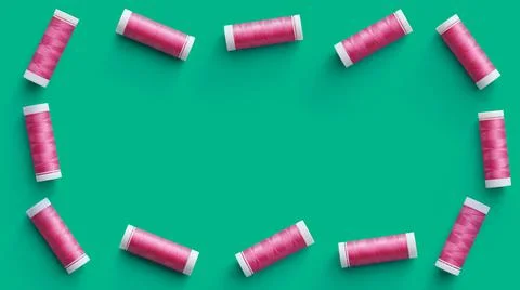 Border of flat-lying spools of pink thread on green background Stock Photos