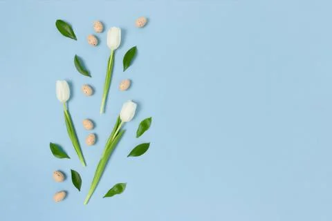 Border frame made of easter eggs and flowers on a blue pastel background. Stock Photos