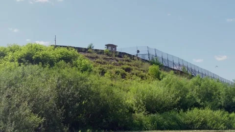 Border security fence with watchtower on green hill in Latvia, tracking shot Stock Footage 340892681