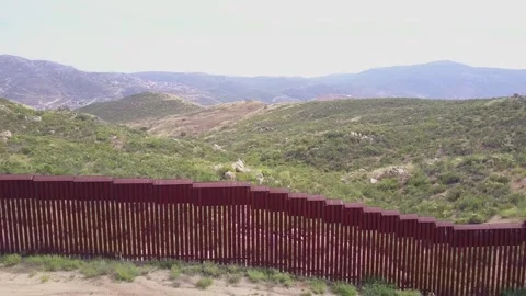 Border wall fence stretching across a rugged, green, mountainous landscape .. Stock Footage 337777648