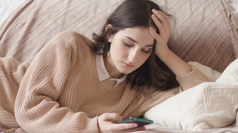 A bored and sad girl uses a smartphone while lying on the couch.  Stock Footage 166845853