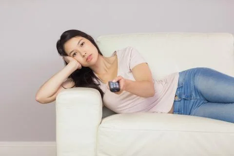 Bored asian girl lying on the couch watching tv Stock Photos