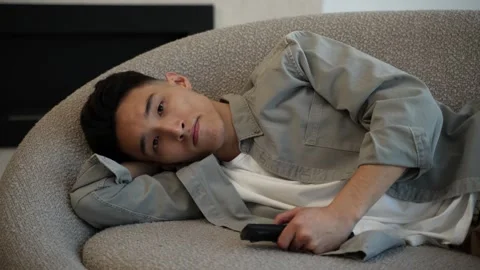 Bored Asian man changes TV channels with remote control Stock Footage 182403051