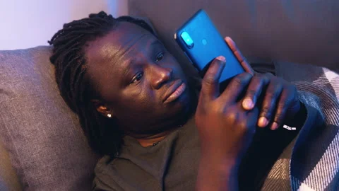 Bored black man using smartphone while resting on the couch Stock Footage 149990833