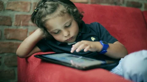 Bored child playing on tablet and sitting on red sofa Stock Footage 41210716