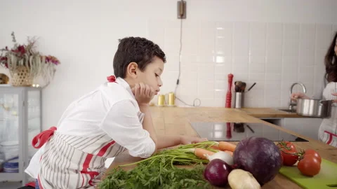 Bored child plays with some vegetables in the kitchen while mother is cooking Video stock 150676436