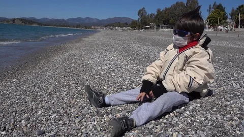 Bored child sits on the beach alone in glasses and mask Video stock 126756099
