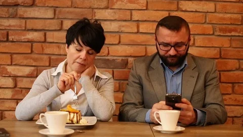 Bored couple sitting by the table at cafe, man writing sms Stock Footage 71746662