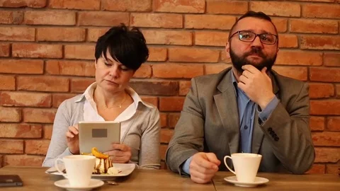 Bored couple sitting by the table at cafe, woman with tablet Stock Footage 71747428