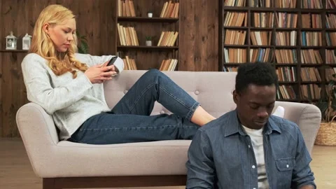 Bored distant mixed race couple ignoring each other. Smartphone addicted couple Stock Footage 153274107