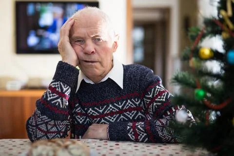 Bored elderly man sitting alone at home table at Christmas Foto stock