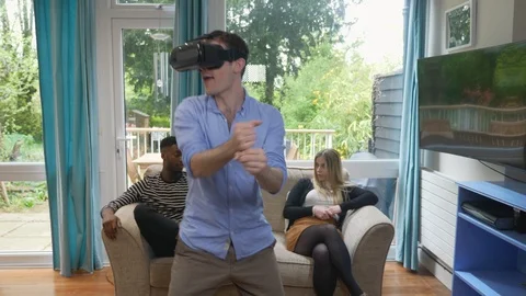 Bored friends watching crazy sword fighting VR man at home headset Stock Footage 89921137