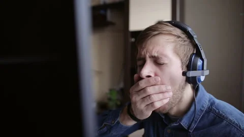 Bored gamer with headset playing in computer online video game and yawning Video stock 99495966