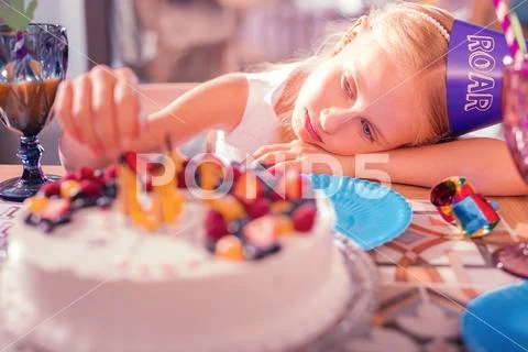 Bored girl leaning on the table and touching candles on her cake Stock Photos