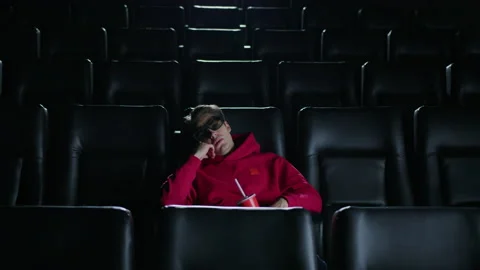 A bored man in 3D glasses drinks soda and watches a movie at the cinema Stock Footage 232939425