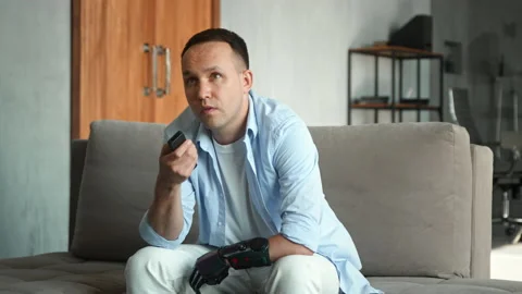 Bored man with hi tech bio limb prothesis switches channels Stock Footage 157348715