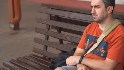 Bored man sits on bench outside and looks at the clock nervous Stock Footage 111859770