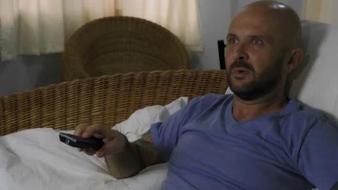 A bored man sits on the couch and switches channels on the TV. Vídeo Stock 145179415