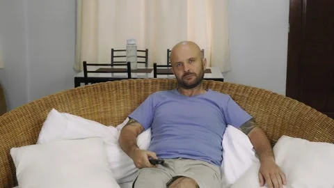 A bored man sits on the couch and switches channels on the TV. Vídeo Stock 145315356