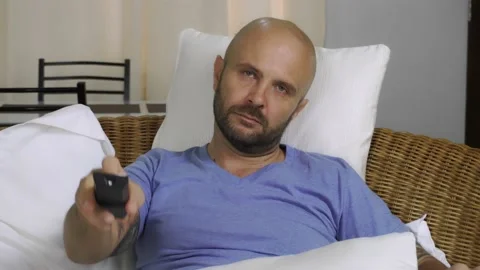 A bored man sits on the couch and switches channels on the TV. Vídeo Stock 145315440
